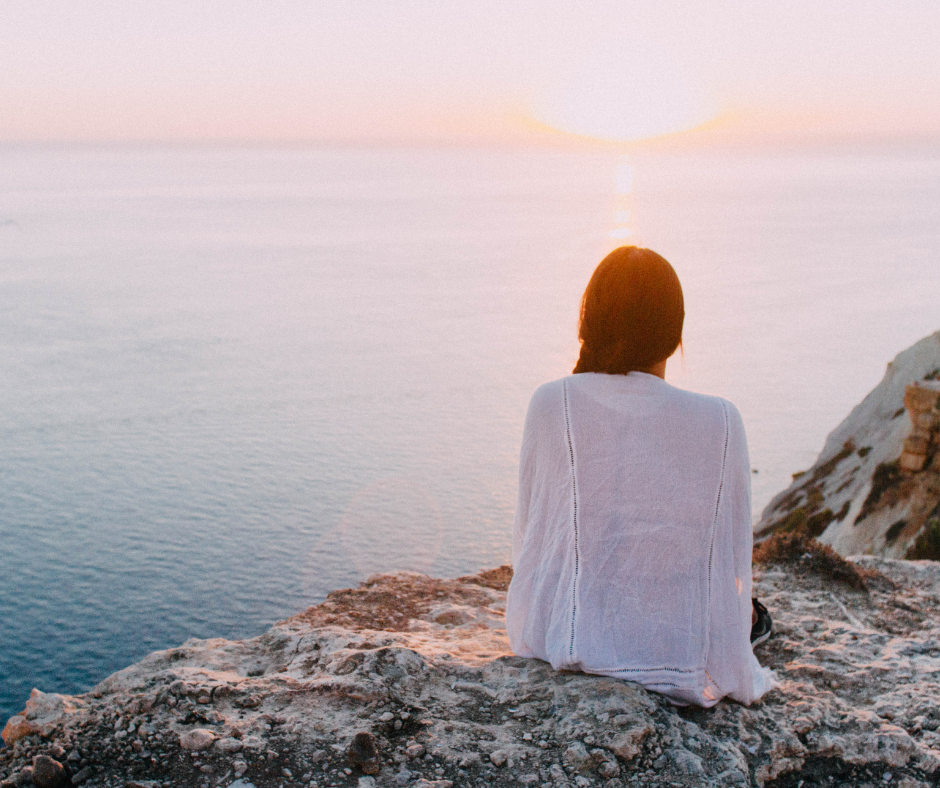 Woman sitting on rocks overlooking the ocean.