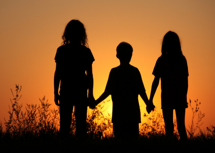 Three children holding hands standing in a field.